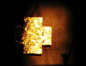Ein goldenes Kreuz vor einem schwarzen Hintergrund, das von der Sonne beschienen wird.